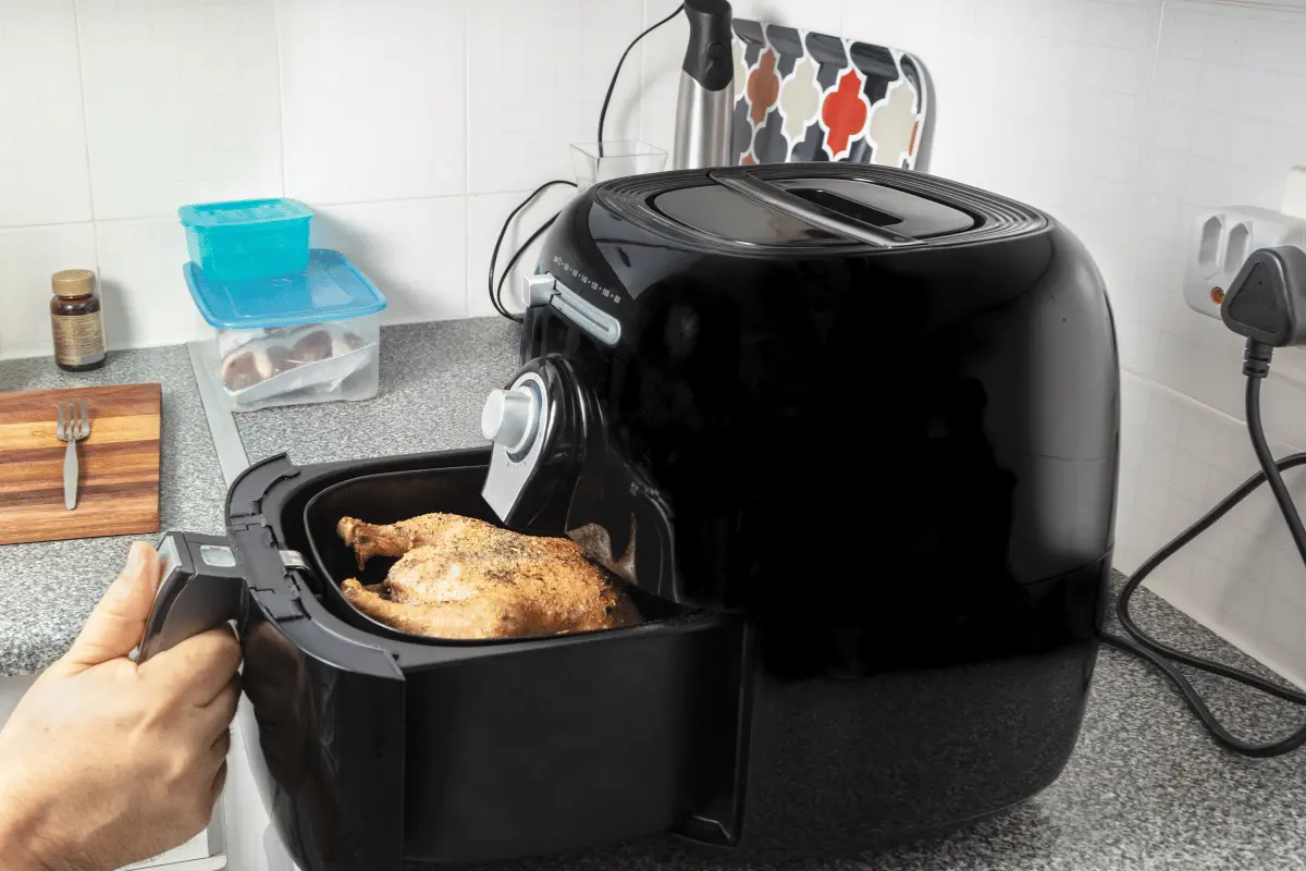 A person cooking a chicken in an air fryer.